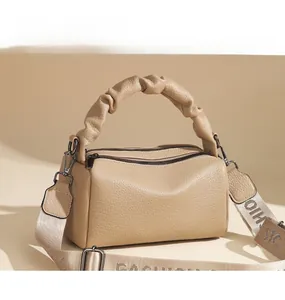 Detail of beige cylinder bag featuring a ruched handle and patterned wide strap