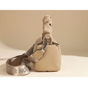 Detail of beige pebble leather bag featuring a ruched handle and woven letter strap