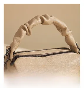 Macro shot of tan handbag showing twisted handle design and litchi grain leather texture