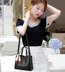 Detail of black lychee leather handbag with floral silk scarf on handle in modern cafe