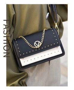 Détail d'un sac bandoulière noir et crème avec boucle en V dorée et rivets décoratifs