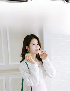 Detail of floral earrings with pearls worn with a white lace shirt and green crossbody bag