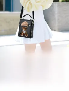 Detail of black faux crocodile leather bag featuring a cute teddy bear embroidery and gold studs