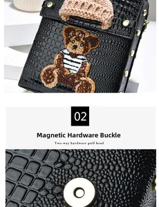 Detail of black crocodile texture bag with embroidered bear and magnetic metal clasp