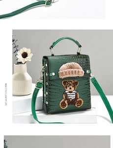 Detail of emerald green crocodile texture handbag with cute bear patch and long shoulder strap