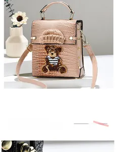 Detail view of pink crocodile pattern crossbody bag with knitted hat and bear embroidery