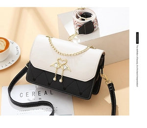 Detail of square crossbody bag featuring golden swan buckle and embroidered strap