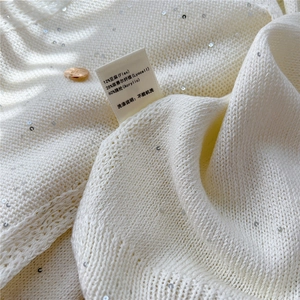 Dettaglio scialle in maglia bianca con paillettes argento e bottone in metallo dorato