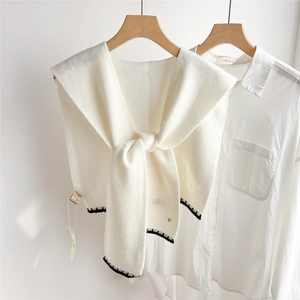 Détail du châle en tricot crème avec bordure festonnée noire sur un col de chemise