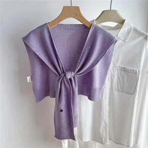 Dettaglio dello scialle in maglia viola con paillettes e ciondoli su camicia bianca