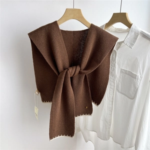 Détail d'un châle tricoté marron foncé avec coutures blanches sur une chemise blanche