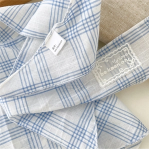 Close-up of blue plaid scarf showing fabric texture, lace patch, and 100% polyester label