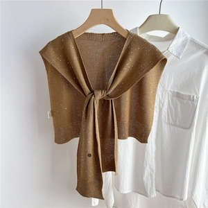 Dettaglio dello scialle in maglia marrone con paillettes e nodo su camicia bianca