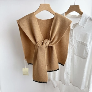 Détail d'un châle en laine tricotée camel avec bordure noire sur une chemise blanche