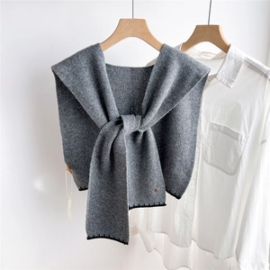 Détail d'un châle en maille gris foncé avec surpiqûres noires et logo doré métallique