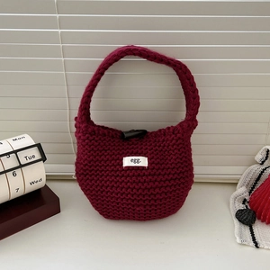 Detail of burgundy knitted tote bag featuring a toggle closure and egg logo label