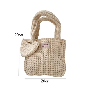 Détail d'un sac cabas en tricot crème avec texture gaufrée, étiquette et breloque cœur