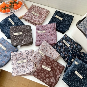 Multiple floral cotton linen square scarves with explore infinity labels on white surface