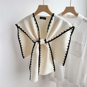 Close-up of cream knitted shawl with black stitching on a hanger for styling detail