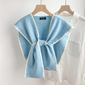 Close-up of light blue knitted shawl with white borders and brand label on white shirt