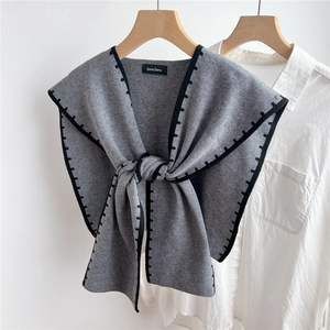 Detail of dark grey knit shawl with black trim and brand tag on a wooden hanger