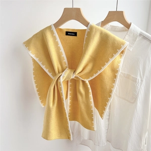 Close-up of yellow knitted shawl wrap with white stitched edges and a bow tie knot