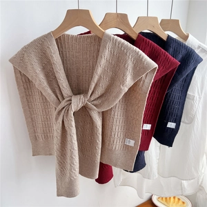 Scialle in maglia grossa crema, blu e rosso con trecce classiche appeso a grucce