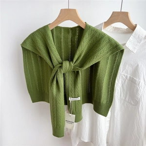 Detail of green knitted hollow pattern shawl with ribbed edge and brand label on a hanger