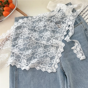 Close-up of white floral lace apron overlay with delicate scalloped edges on denim jeans