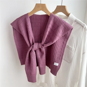 Dettaglio dello scialle in maglia viola con trecce e fiocco annodato su camicia bianca