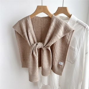 Dettaglio dello scialle in maglia beige a trecce su camicia bianca in cotone e gruccia