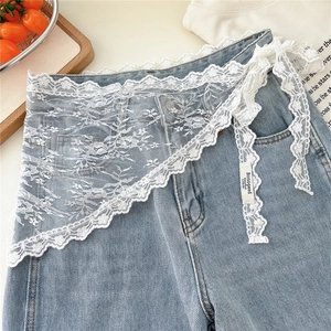 Detailed close-up of white floral lace waist accessory with scalloped edges on denim
