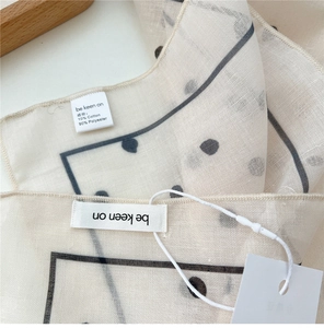 Detailed macro shot of 10% cotton polka dot scarf texture with stitched hem and brand tag