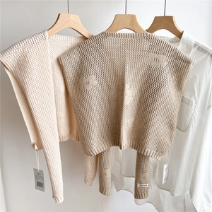 Detail of knitted floral shawl vest showing hollow patterns and ribbed edges on a hanger