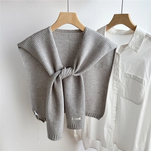 Detail of grey knitted shawl with HELLO ACHY label on a white shirt and wooden hanger