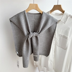 Close-up of gray hollowed knit shawl cape with brand label on white shirt