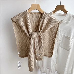 Detail of beige knit shawl showing intricate hollow weave texture and brand label on a hanger