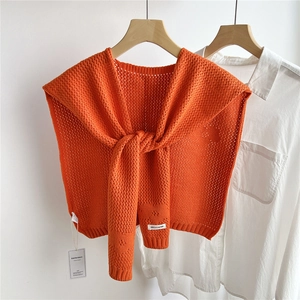 Detail of bright orange hollow-out knit shawl over white shirt with visible texture