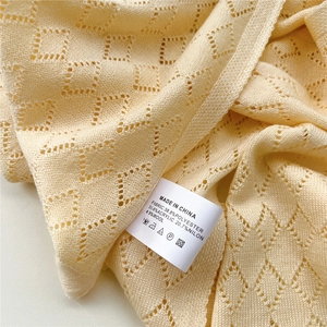 Detailansicht des cremefarbenen Strickschals mit Rautenmuster und dem Pflegeetikett