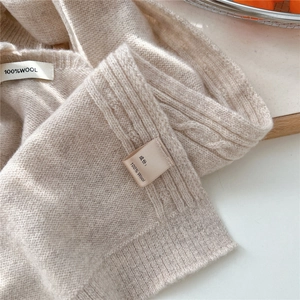 Detail of beige wool knit shawl showing soft cable textures and material labels