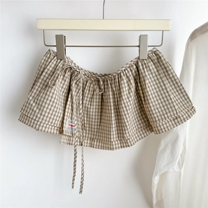 Detail of plaid pleated skirt layering piece with drawstring and woven label decoration