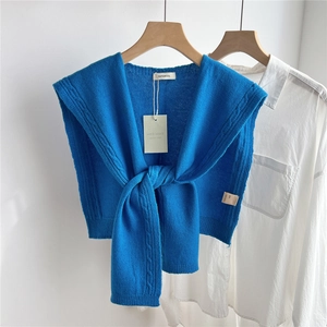 Detailed close-up of blue cable-knit wool shawl with front twist knot on white shirt