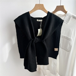 Detail of black cable-knit 100% wool shawl layered over a white long-sleeve shirt