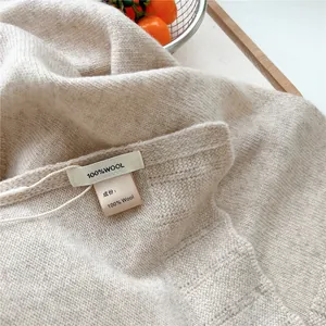 Close-up of beige knitted wool shawl showing fine 100% wool texture and official material tag