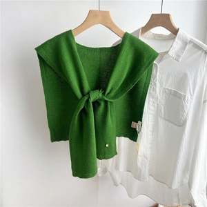 Detail of green knit wool shawl with decorative knot styling on a white shirt