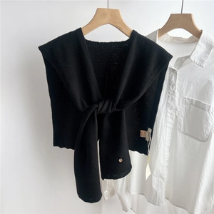 Detail of black wool knitted shawl tied over white shirt with fine metal buckle
