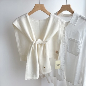 Detail of white 100% wool knitted shawl with a round button over a long sleeve shirt