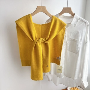 Detail of yellow wool knit shawl tied over a white shirt on a wooden hanger