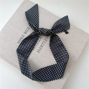 Gros plan d'un ruban en soie noir à pois blancs noué en boucle sur une texture en lin