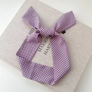Détail d'un foulard en soie violet à pois noué en nœud sur un support texturé chic